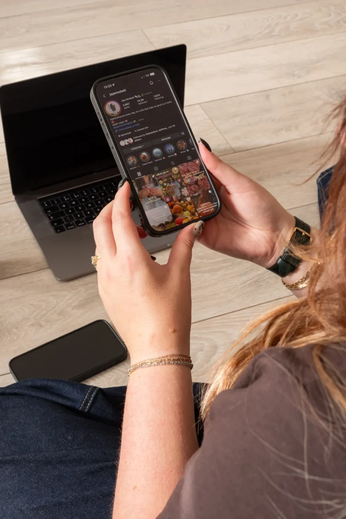 Jaye reviewing her Instagram profile on a phone beside her laptop