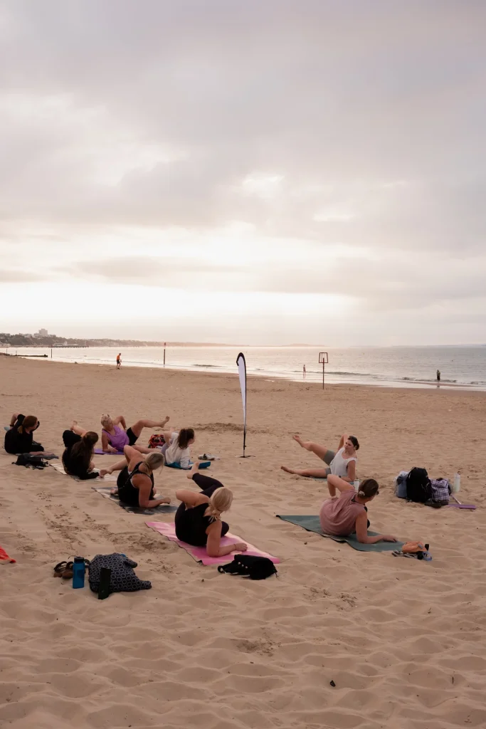 Beach Pilates class exercising on mats beside the sea