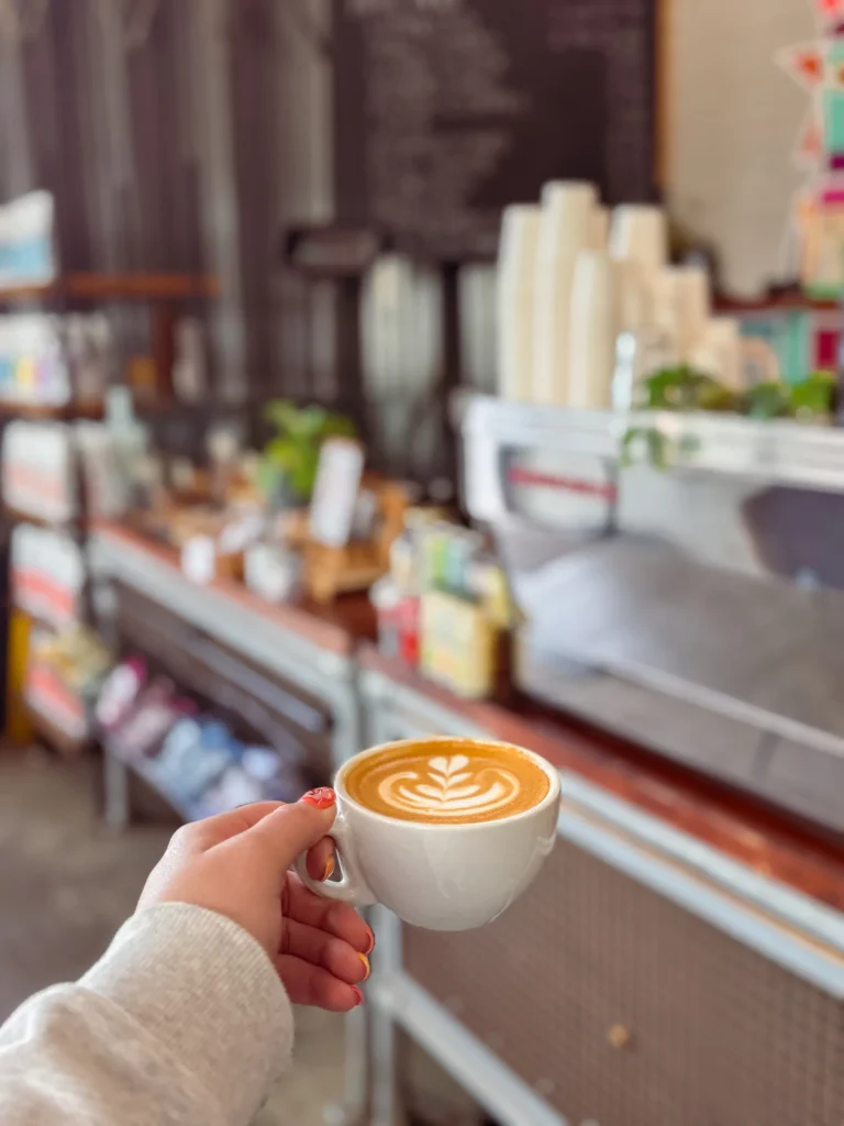 Hand holding a coffee with latte art inside the shop