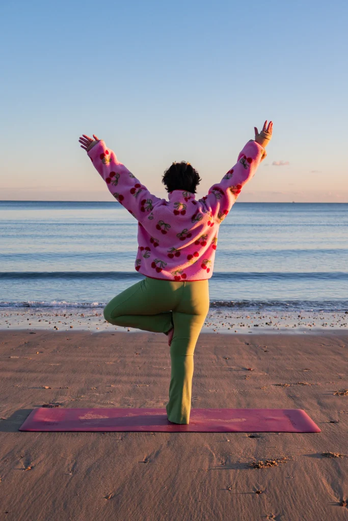 Person balancing on one leg with arms raised at the beach