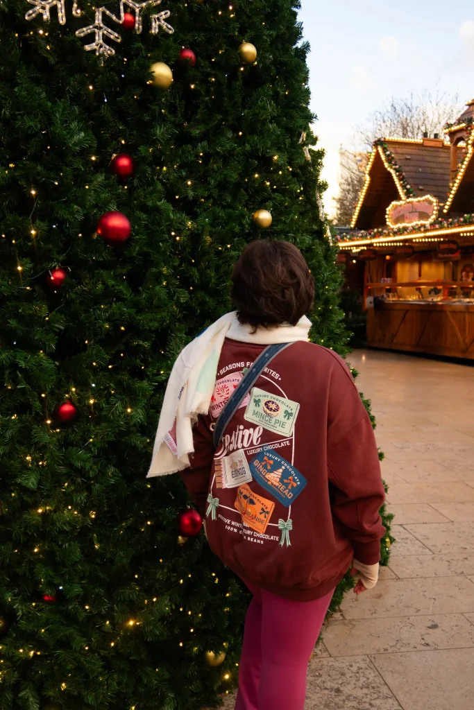 Person standing beside a decorated Christmas tree at a market