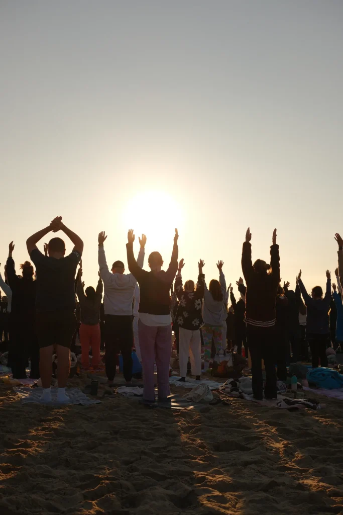 Participants raising their arms towards the sunrise on the beach