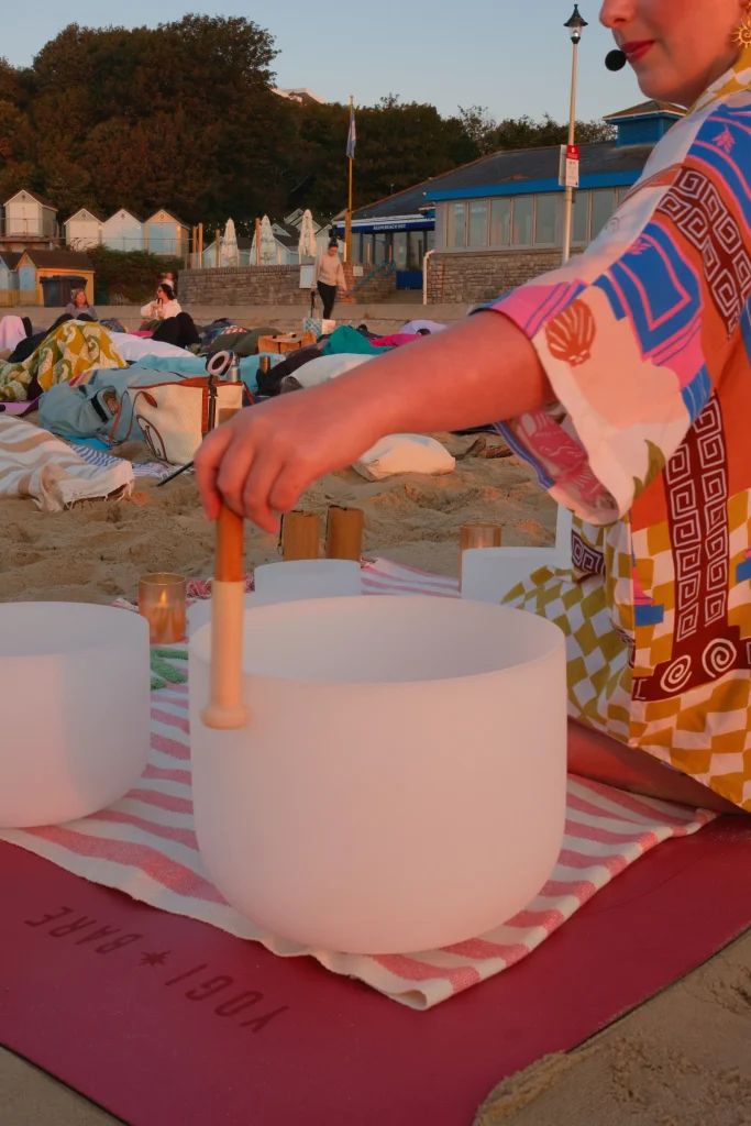 Sound bath facilitator playing a singing bowl beside resting participants