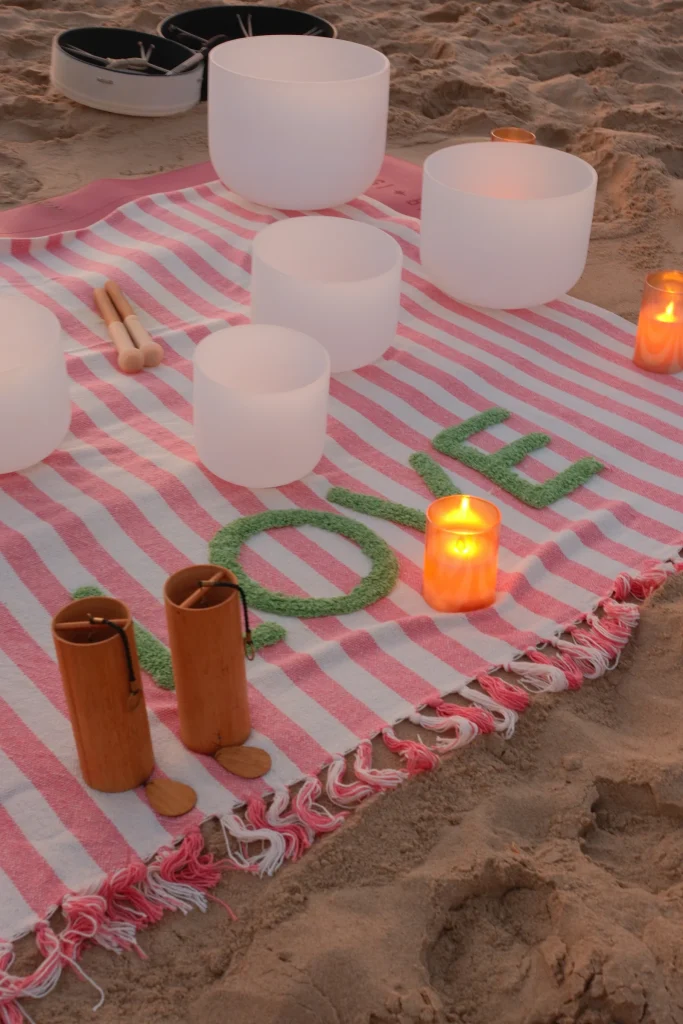 Singing bowls and candles arranged on a striped blanket in the sand